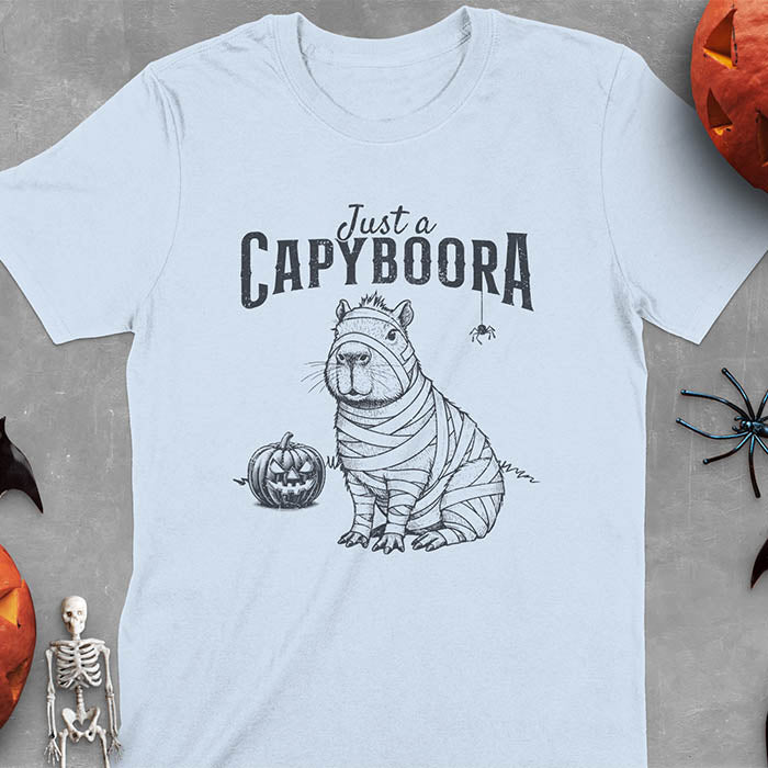 Light blue t-shirt with a Halloween mummy capyboora t-shirt featuring cute capybara wrapped in white bandages with spooky Halloween design
