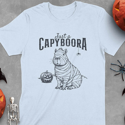 Light blue t-shirt with a Halloween mummy capyboora t-shirt featuring cute capybara wrapped in white bandages with spooky Halloween design