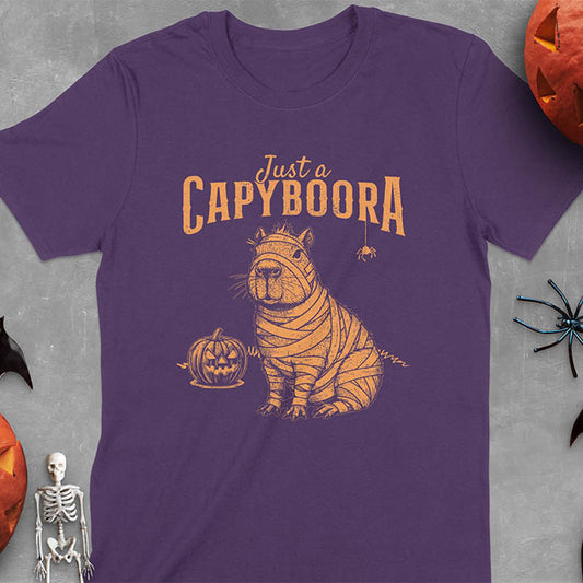 Purple t-shirt with a Halloween mummy capyboora t-shirt featuring cute capybara wrapped in white bandages with spooky Halloween design