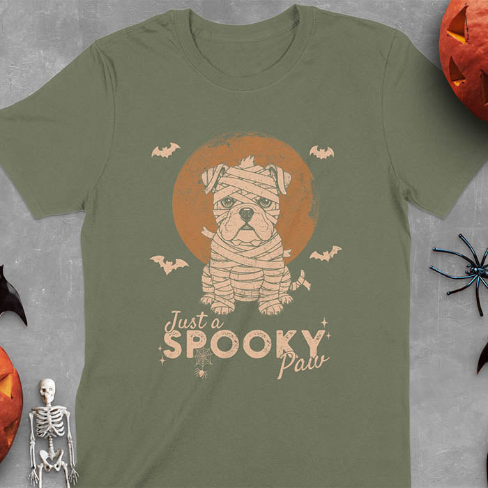Military Green t-shirt featuring adorable mummy bulldog puppy with white bandages and big eyes, Halloween design with 'Just a SPOOKY PAW' text below