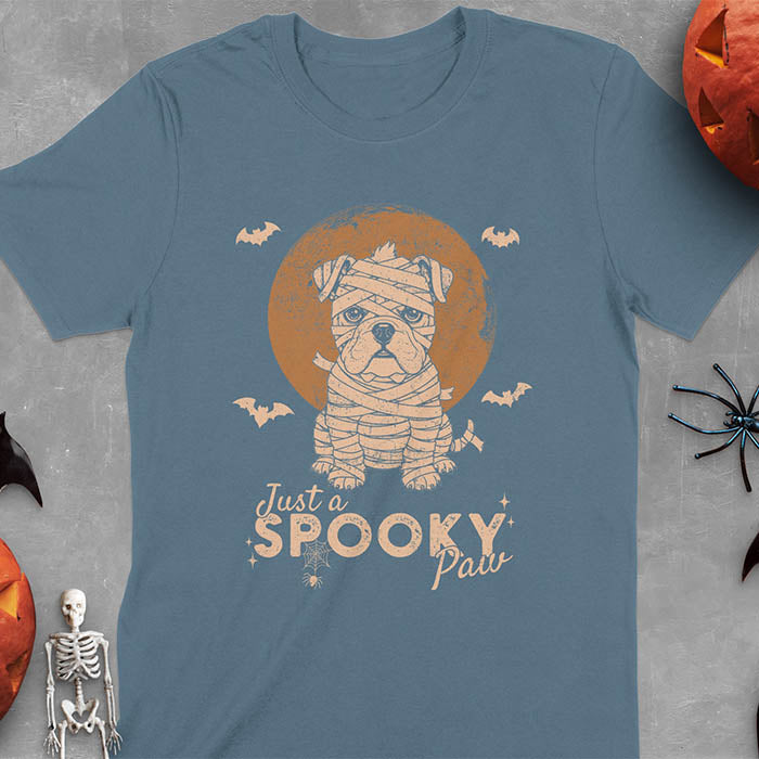 Indigo Blue t-shirt featuring adorable mummy bulldog puppy with white bandages and big eyes, Halloween design with 'Just a SPOOKY PAW' text below