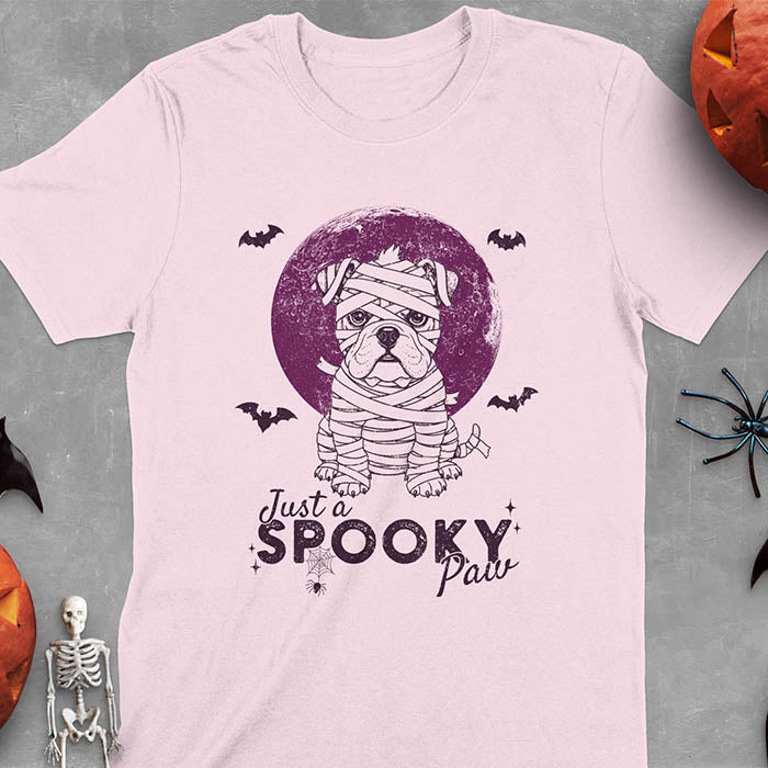 Light Pink t-shirt featuring adorable mummy bulldog puppy with white bandages and big eyes, Halloween design with 'Just a SPOOKY PAW' text below