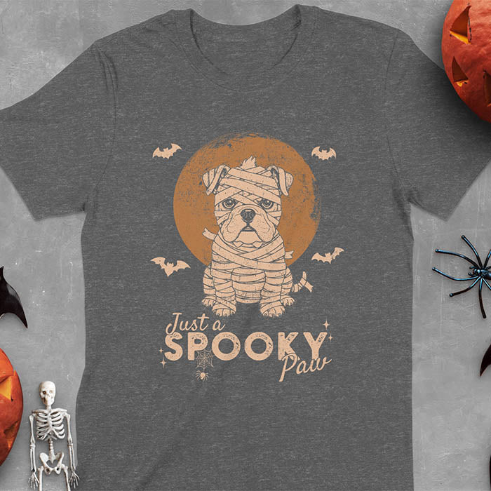 Dark heather t-shirt featuring adorable mummy bulldog puppy with white bandages and big eyes, Halloween design with 'Just a SPOOKY PAW' text below