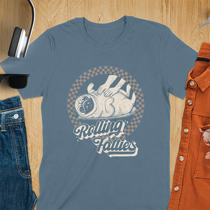 Indigo Blue t-shirt with 'Rolling Fatties' text and illustration of chubby pug lying on its back inside black and white checkered circle border, with human hands reaching toward pug's belly