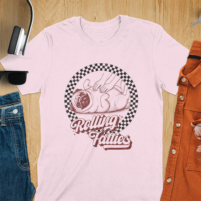 Light Pink t-shirt with 'Rolling Fatties' text and illustration of chubby pug lying on its back inside black and white checkered circle border, with human hands reaching toward pug's belly