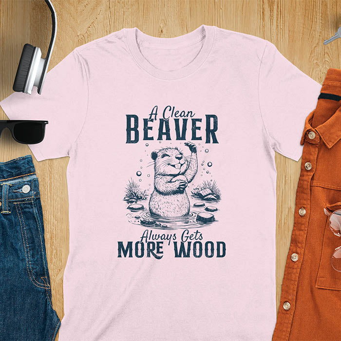 Light Pink t-shirt featuring illustrated beaver bathing in water with text 'A Clean Beaver Always Gets More Wood' - adult humor meme design with cartoon beaver surrounded by water bubbles and tree stumps