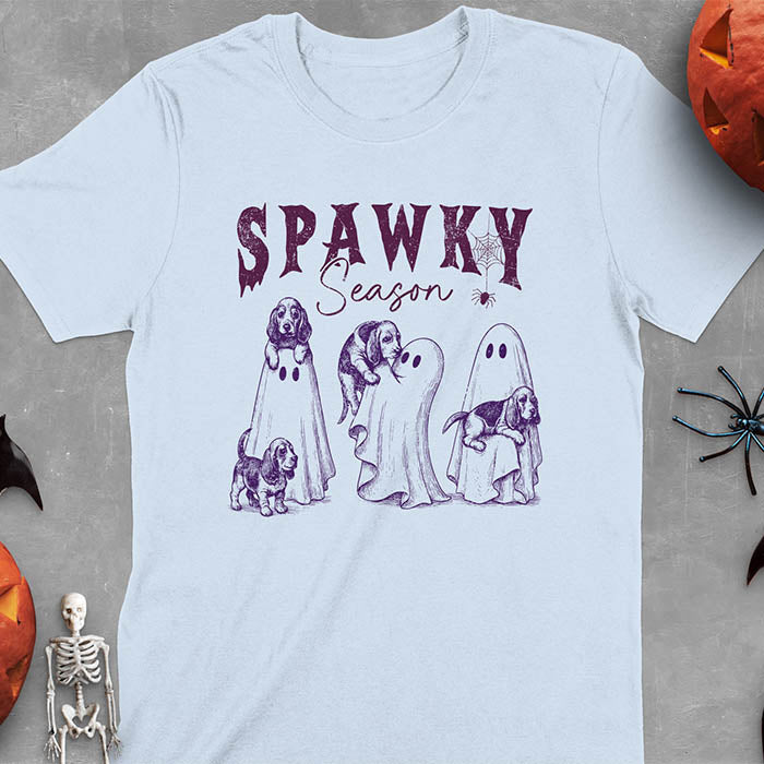 Light blue Halloween T-shirt featuring 'SPAWKY Season' text with cute ghosts carrying Basset Hound puppies, designed in purple ink with playful Halloween theme