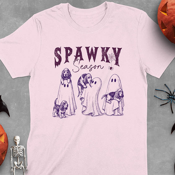 Light pink Halloween T-shirt featuring 'SPAWKY Season' text with cute ghosts carrying Basset Hound puppies, designed in purple ink with playful Halloween theme