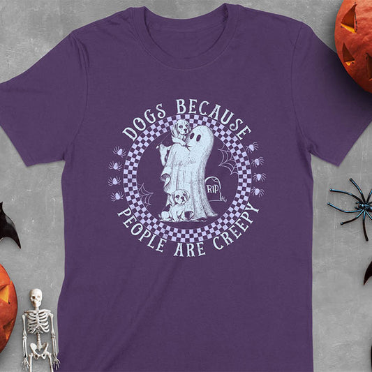 Purple Halloween t-shirt featuring a cute ghost holding a beagle puppy with another beagle sitting on the ground next to a tombstone marked 'RIP', surrounded by spiders in a circular checkered border design with text 'DOGS BECAUSE PEOPLE ARE CREEPY'