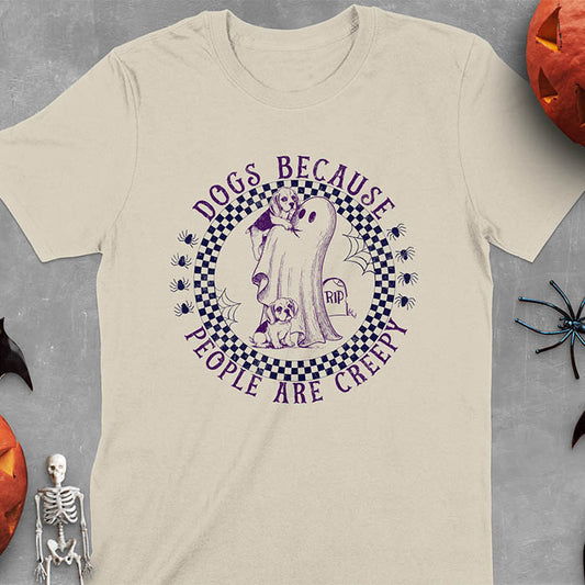 Sand colored Halloween t-shirt featuring a cute ghost holding a beagle puppy with another beagle sitting on the ground next to a tombstone marked 'RIP', surrounded by spiders in a circular checkered border design with text 'DOGS BECAUSE PEOPLE ARE CREEPY'