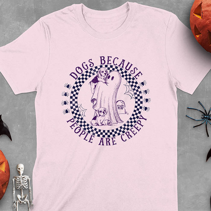 Light pink Halloween t-shirt featuring a cute ghost holding a beagle puppy with another beagle sitting on the ground next to a tombstone marked 'RIP', surrounded by spiders in a circular checkered border design with text 'DOGS BECAUSE PEOPLE ARE CREEPY'