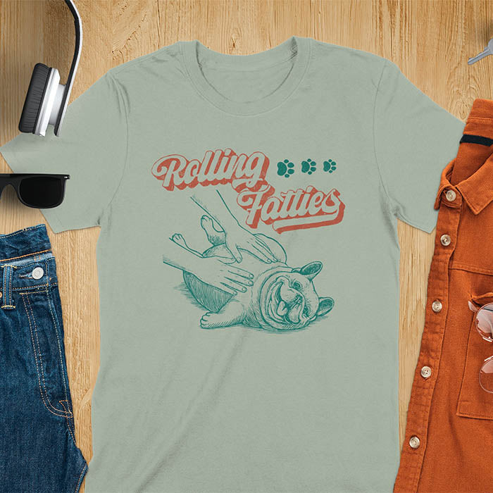 Sage green t-shirt with Rolling Fatties script text and French Bulldog being petted by human hands in line drawing style.