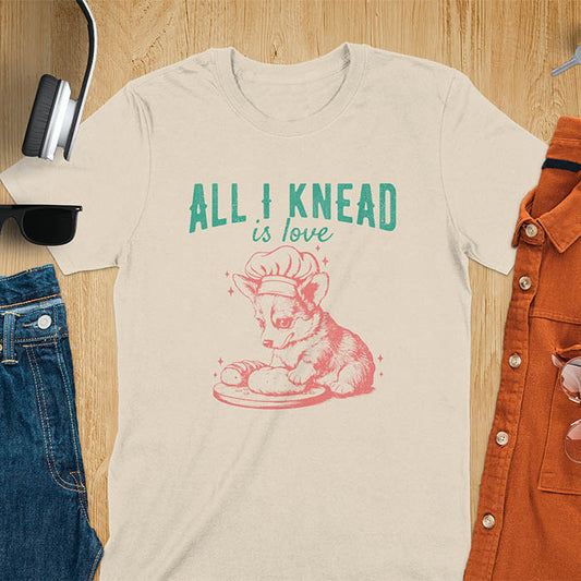 Sand color t-shirt with a Cute corgi baking t-shirt featuring cartoon dog in chef hat with All I Knead Is Love text
