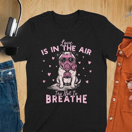 Anti-Valentine's Day pug wearing pink gas mask graphic tee with Love is in the Air Try Not to Breathe text and hearts on black shirt