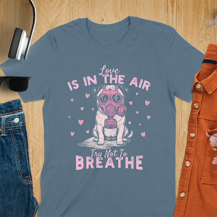 Anti-Valentine's Day pug wearing pink gas mask graphic tee with Love is in the Air Try Not to Breathe text and hearts on indigo blue shirt