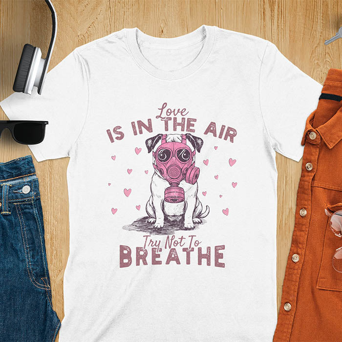 Anti-Valentine's Day pug wearing pink gas mask graphic tee with Love is in the Air Try Not to Breathe text and hearts on white shirt