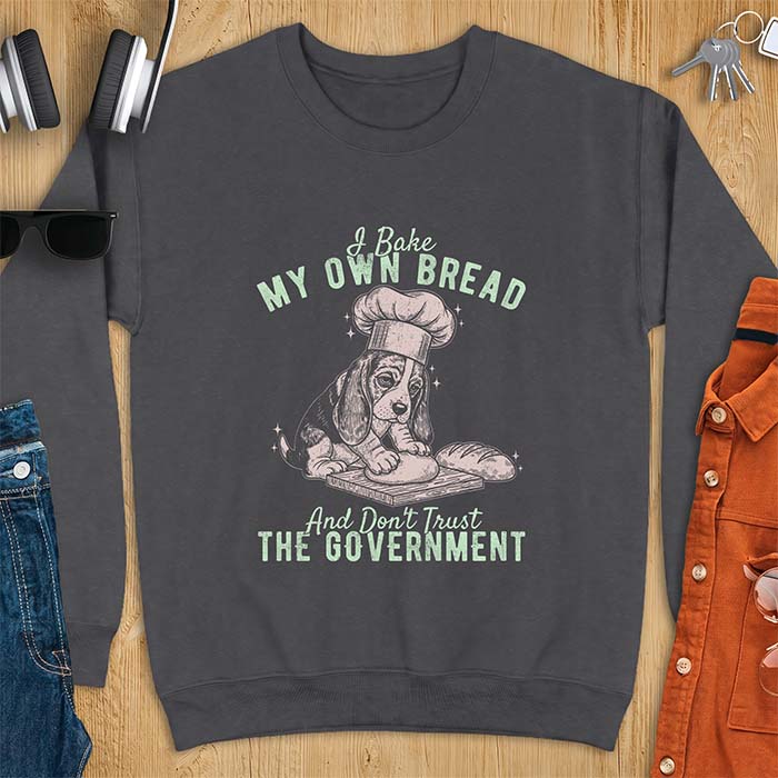 Dark Heather sweatshirt with a graphic of a basset hound in a chef's hat kneading dough beside a loaf of bread and the text I Bake My Own Bread And Don't Trust The Government