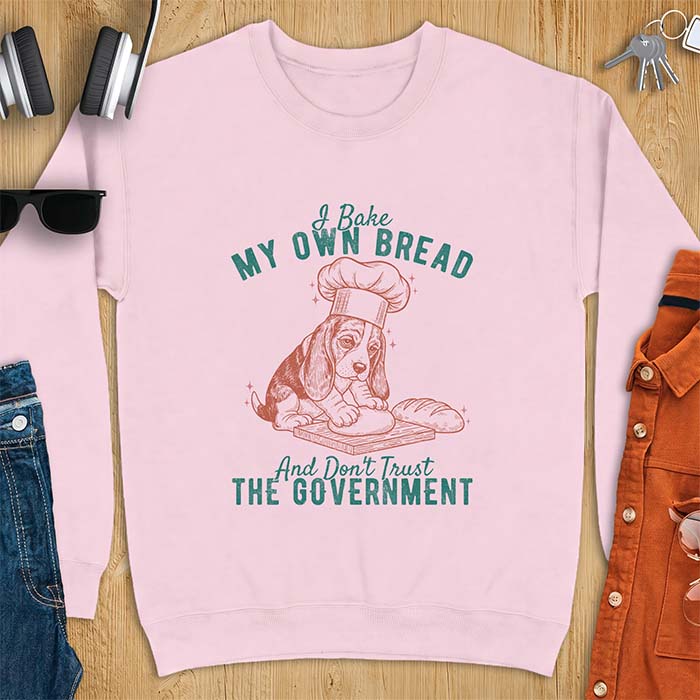 Light Pink sweatshirt with a graphic of a basset hound in a chef's hat kneading dough beside a loaf of bread and the text I Bake My Own Bread And Don't Trust The Government