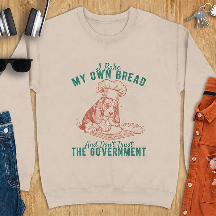 Sand sweatshirt with a graphic of a basset hound in a chef's hat kneading dough beside a loaf of bread and the text I Bake My Own Bread And Don't Trust The Government