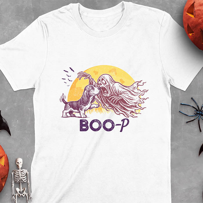 White t-shirt with a Halloween graphic of a Basset Hound puppy booping a screaming ghost's nose as it reaches out with a skeletal hand with bats flying past a glowing moon and the text Boo-P underneath