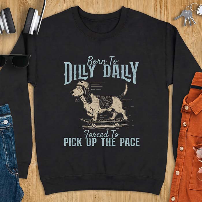 Black sweatshirt with a graphic of a basset hound in a skater helmet riding a skateboard with long ears flying back, printed with the text Born To Dilly Dally, Forced To Pick Up The Pace