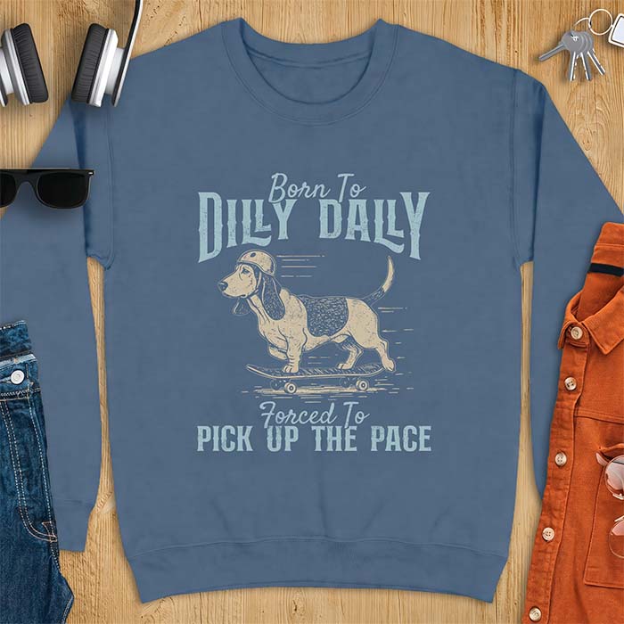 Indigo Blue sweatshirt with a graphic of a basset hound in a skater helmet riding a skateboard with long ears flying back, printed with the text Born To Dilly Dally, Forced To Pick Up The Pace