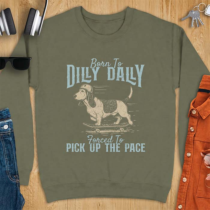 Military Green sweatshirt with a graphic of a basset hound in a skater helmet riding a skateboard with long ears flying back, printed with the text Born To Dilly Dally, Forced To Pick Up The Pace