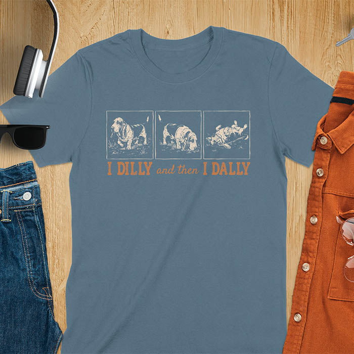 Basset hound comic strip tee — three panels: walking, sniffing, flopped over — with text "I DILLY and then I DALLY" in bold retro typography, indigo blue