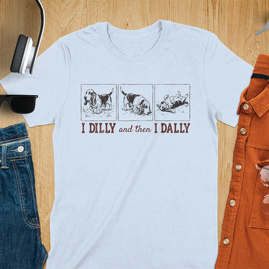 Basset hound comic strip tee — three panels: walking, sniffing, flopped over — with text "I DILLY and then I DALLY" in bold retro typography, light blue
