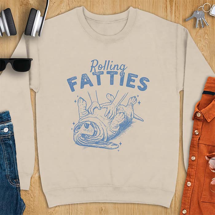Sand sweatshirt with a graphic of a basset hound lying on its back while a pair of hands knead its rolled up folds like dough and the text Rolling Fatties