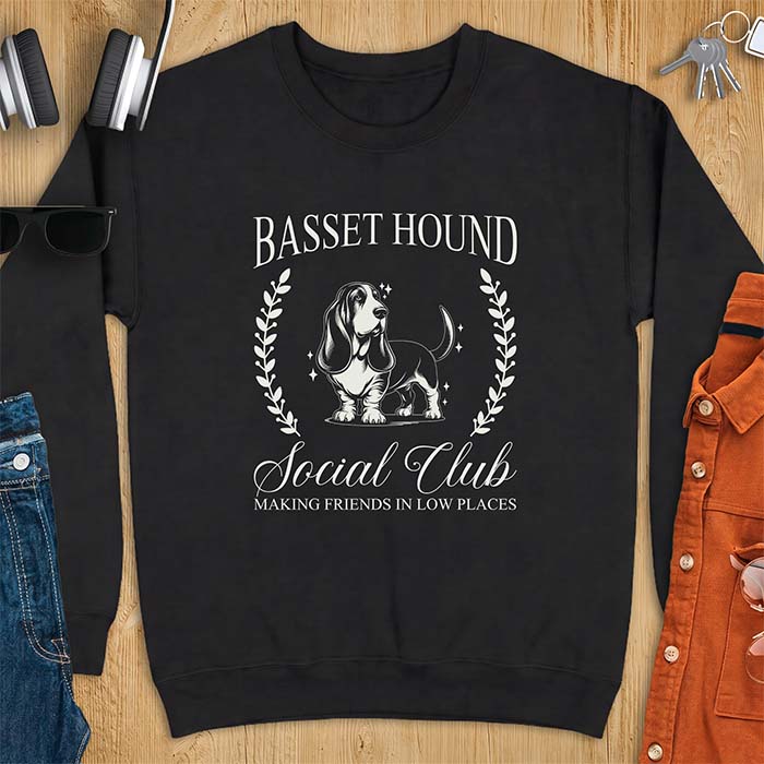 Black sweatshirt with a vintage crest graphic of a basset hound standing inside a laurel wreath and the text Basset Hound, Social Club and Making Friends In Low Places
