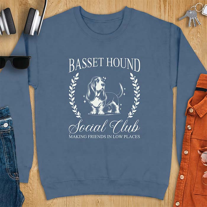 Indigo Blue sweatshirt with a vintage crest graphic of a basset hound standing inside a laurel wreath and the text Basset Hound, Social Club and Making Friends In Low Places