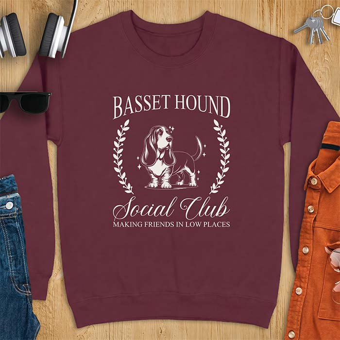 Maroon sweatshirt with a vintage crest graphic of a basset hound standing inside a laurel wreath and the text Basset Hound, Social Club and Making Friends In Low Places