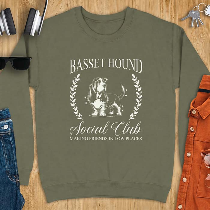 Military Green sweatshirt with a vintage crest graphic of a basset hound standing inside a laurel wreath and the text Basset Hound, Social Club and Making Friends In Low Places