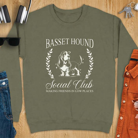 Military Green sweatshirt with a vintage crest graphic of a basset hound standing inside a laurel wreath and the text Basset Hound, Social Club and Making Friends In Low Places