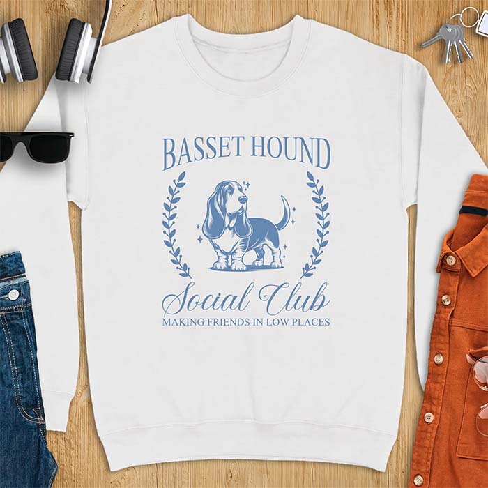 White sweatshirt with a vintage crest graphic of a basset hound standing inside a laurel wreath and the text Basset Hound, Social Club and Making Friends In Low Places