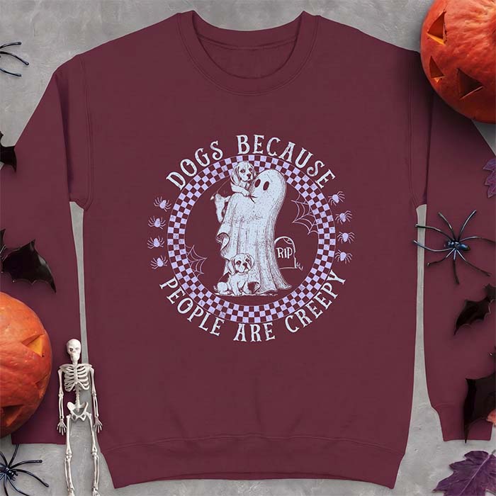 Maroon sweatshirt with a Halloween graphic of two Beagle puppies peeking around a classic bedsheet ghost inside a checkerboard circle with spiders and cobwebs, and the text Dogs Because People Are Creepy