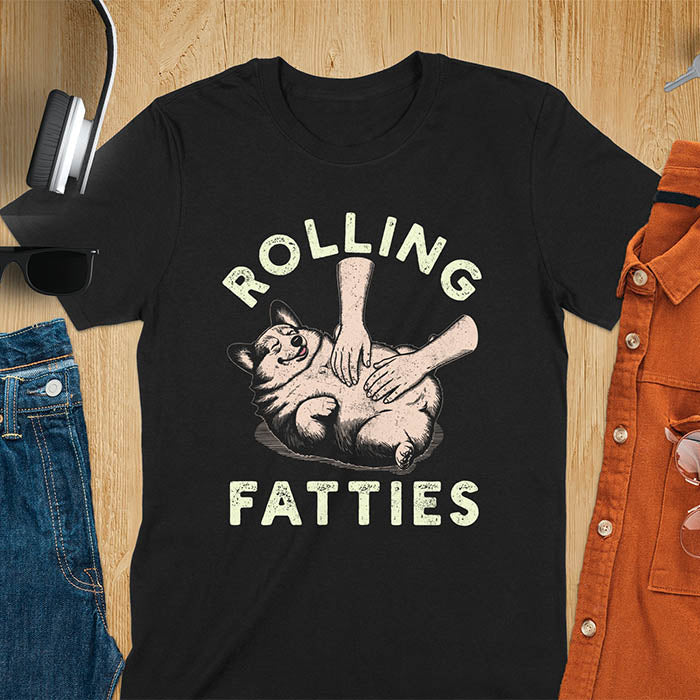 Chubby corgi illustration enjoying tummy rubs with Rolling Fatties text in textured lettering on black tee