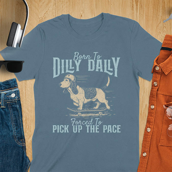 Basset hound wearing helmet on skateboard with Born To Dilly Dally Forced To Pick Up The Pace lettering on indigo blue tee