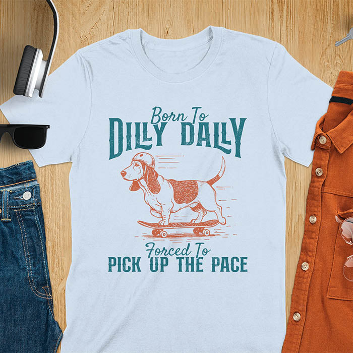 Basset hound wearing helmet on skateboard with Born To Dilly Dally Forced To Pick Up The Pace lettering on light blue tee