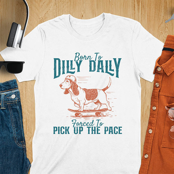 Basset hound wearing helmet on skateboard with Born To Dilly Dally Forced To Pick Up The Pace lettering on white tee