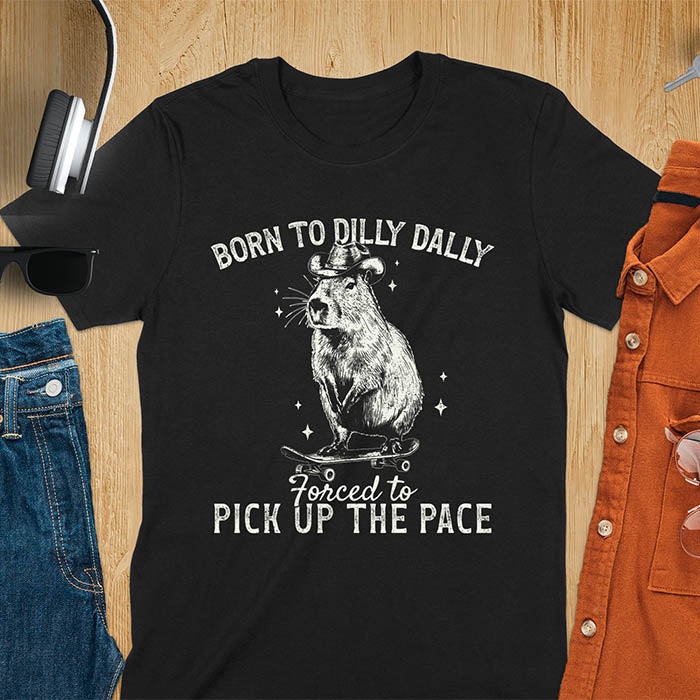 Black color tee featuring a Capybara in a cowboy hat on a skateboard. Born to Dilly Dally and Forced to Pick Up the Pace text. Distressed style.