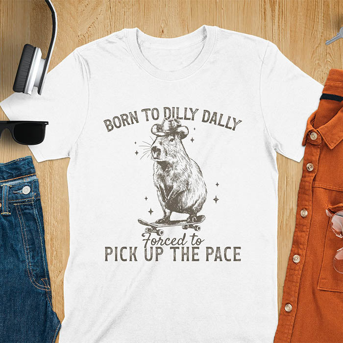 White color tee featuring a Capybara in a cowboy hat on a skateboard. Born to Dilly Dally and Forced to Pick Up the Pace text. Distressed style.