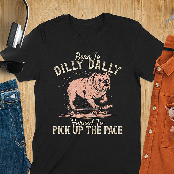 Grumpy bulldog on skateboard illustration with Born To Dilly Dally text and Forced To Pick Up The Pace slogan on black tee
