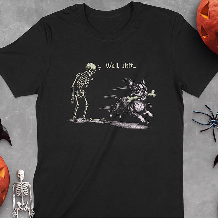 Black t-shirt with a Halloween graphic of a skeleton looking down at its fallen arm on the ground while a Boston Terrier runs past with a bone in its mouth and the text Well, shit...
