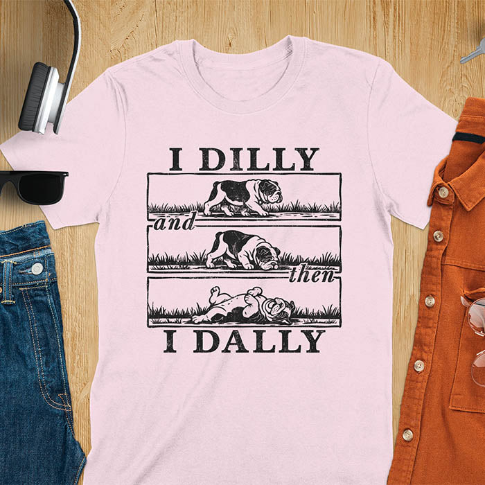 Light pink t-shirt with vintage comic strip graphic of a bulldog walking, rolling, then lying belly-up with text I Dilly and then I Dally