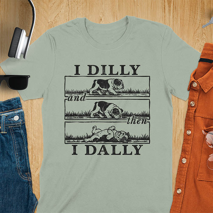 Sage green t-shirt with vintage comic strip graphic of a bulldog walking, rolling, then lying belly-up with text I Dilly and then I Dally