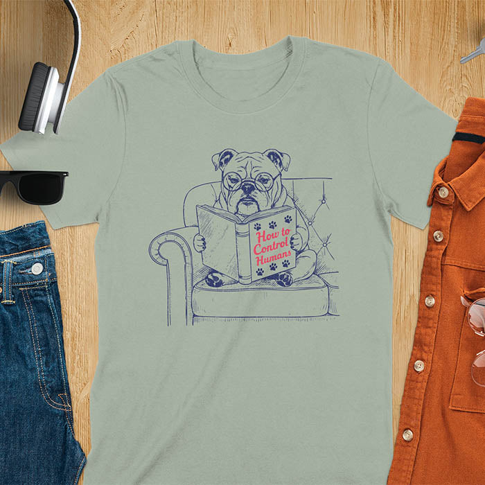 Sage green t-shirt with vintage bulldog illustration reading 'How to Control Human' book on couch - retro graphic design with humor