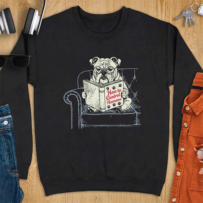 Black sweatshirt with a graphic of a bespectacled English Bulldog sitting in a tufted armchair reading a book titled How to Control Humans, decorated with paw prints