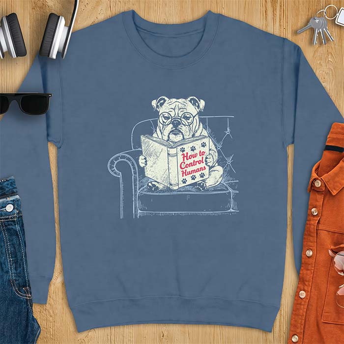 Indigo Blue sweatshirt with a graphic of a bespectacled English Bulldog sitting in a tufted armchair reading a book titled How to Control Humans, decorated with paw prints